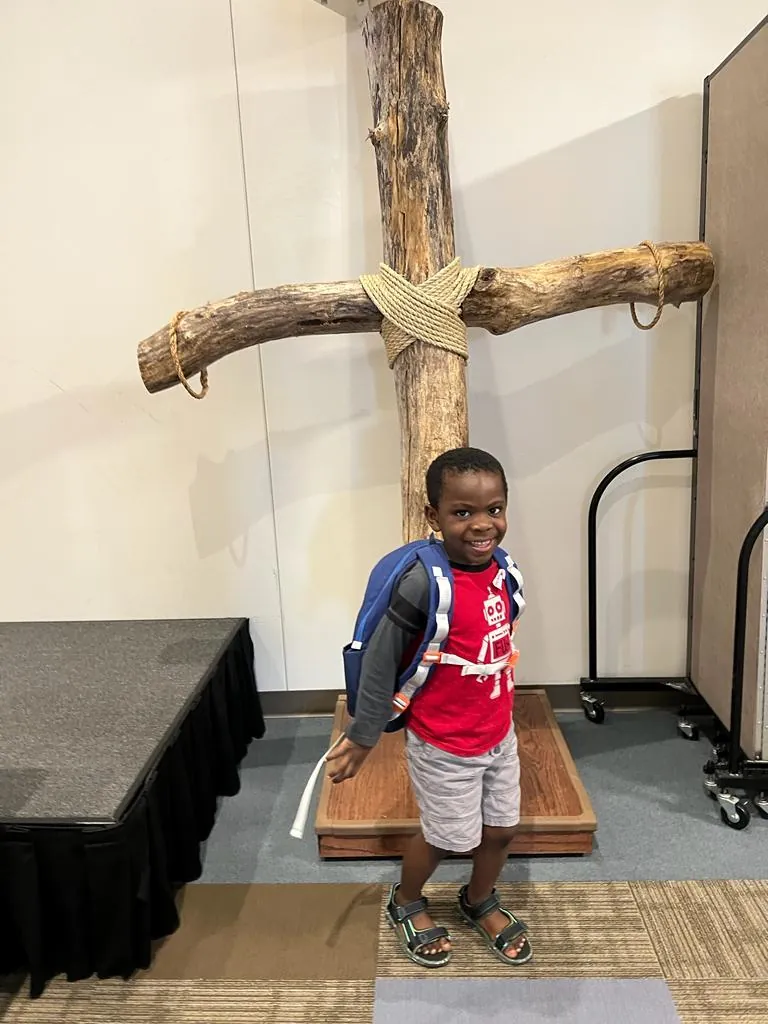 A young boy at church in front of a wooden cross