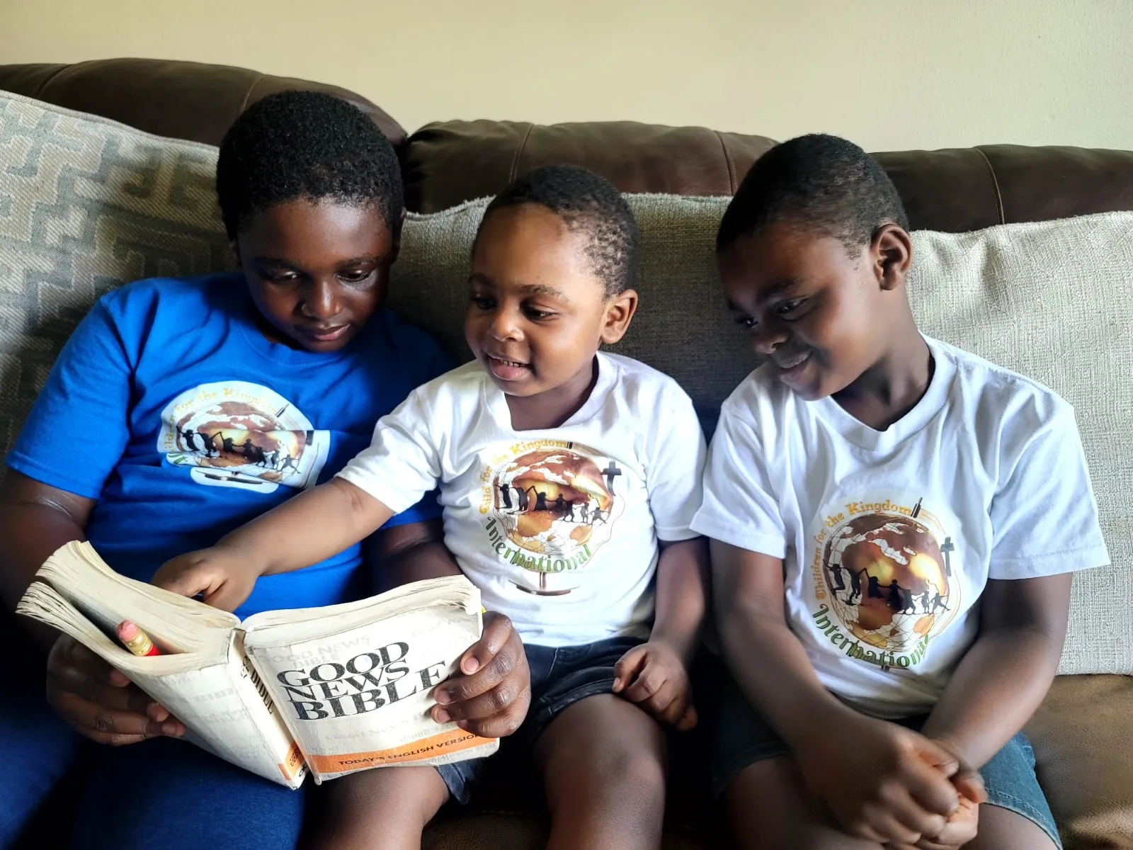 Three children in Children for the Kingdom t-shirts reading a Bible together